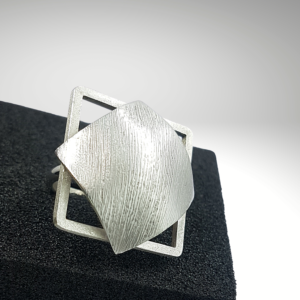 Square silver ring with a domed plate and a frame sitting on the black ring holder