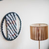 Cassandra Sabo’s ‘West Coast 8’ woven circular textile wall-hanging from her West Coast Collection hung on the wall beside a table lamp