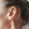 Simple Sterling silver earrings are worn on the earlobe of the white woman.
