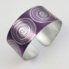 Purple aluminium women's suffrage cuff with a scroll pattern all the way around it in a silvery colour