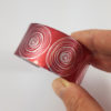 red aluminium cuff with a silvery scroll pattern held in a hand