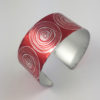 red aluminium cuff with scroll patterns in a silvery colour seen from above