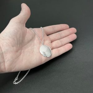 hand holding a round pendant in silver on a black background